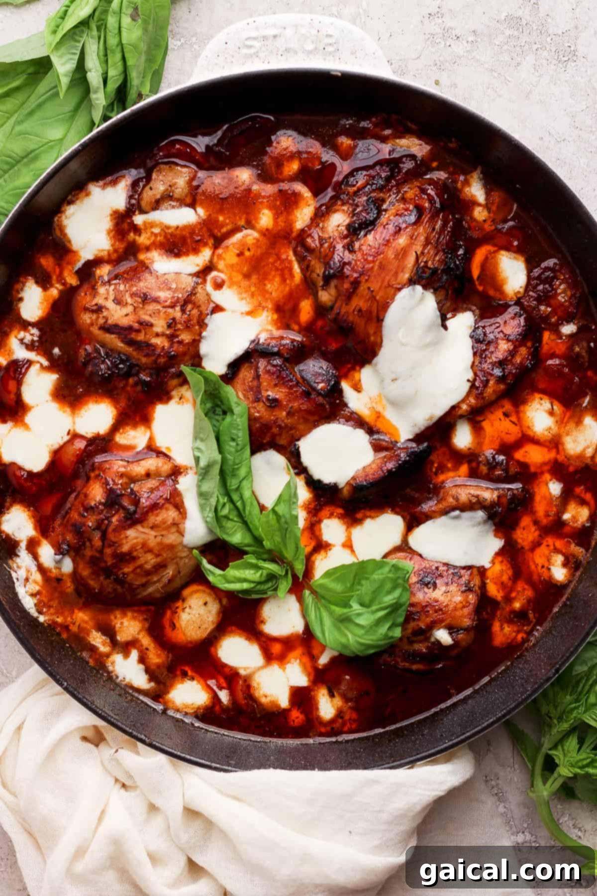 Rich Balsamic Glazed Chicken Thighs 2 A skillet with chicken in a sauce with basil leaves.