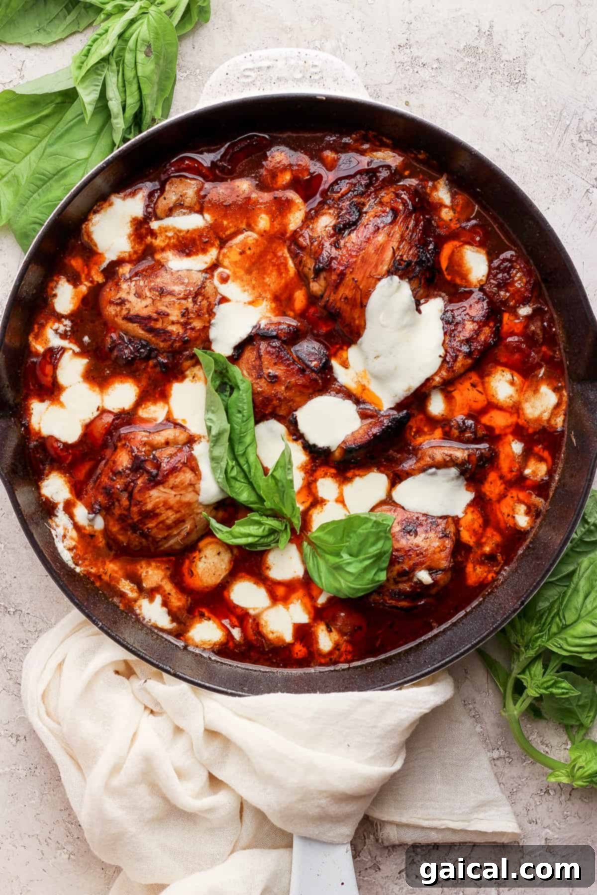 Rich Balsamic Glazed Chicken Thighs 7 A skillet with chicken in a sauce with basil leaves.