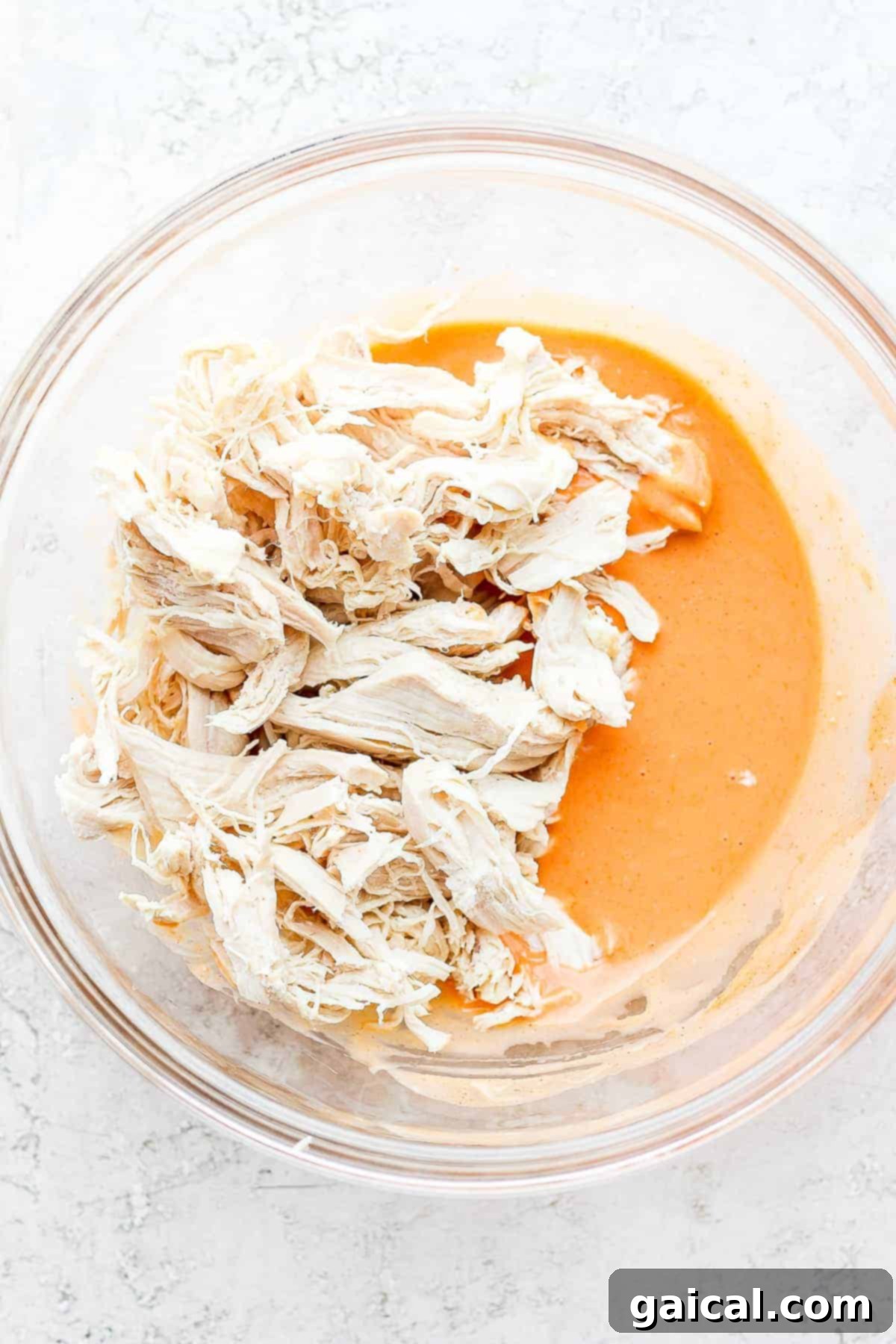 Buffalo Shredded Chicken Mixture Shredded chicken generously coated in our creamy and spicy buffalo sauce, presented in a mixing bowl and ready for assembly into wraps.