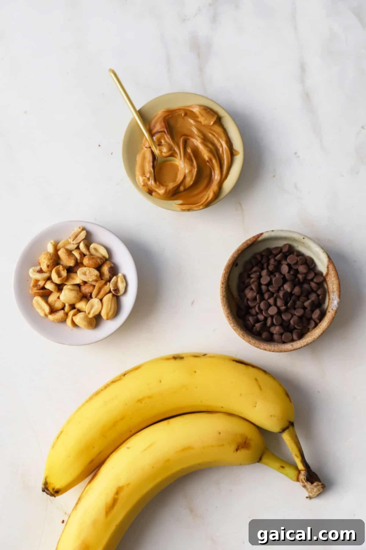Air Fryer Roasted Banana Split 3 Ripe bananas, creamy peanut butter, mini chocolate chips, and chopped peanuts arranged on a wooden surface, ready for recipe preparation.