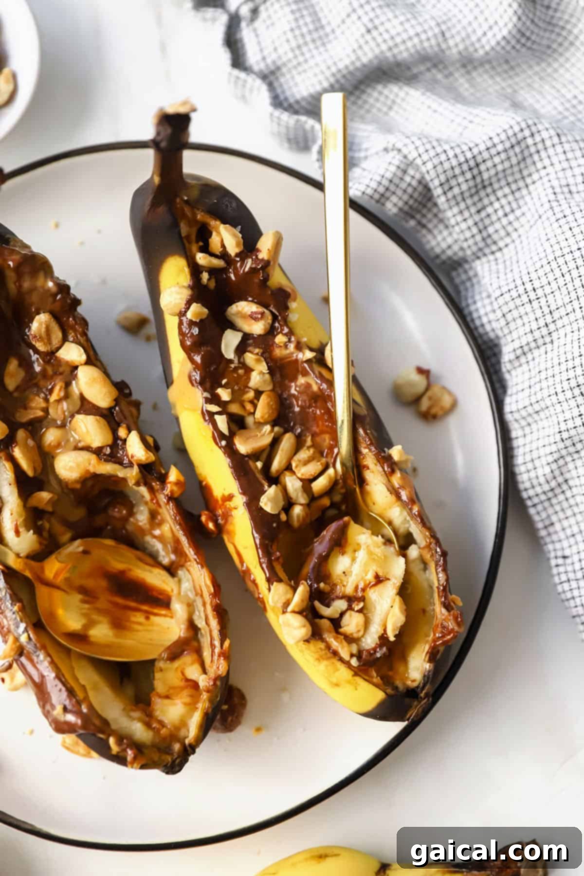 Air Fryer Roasted Banana Split 4 Two air fryer banana halves, stuffed with peanut butter and chocolate, topped with chopped peanuts and sea salt on a plate.