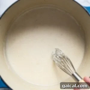Velvety Broccoli Pasta 8 A person whisking a liquid in a pan, thickening the sauce.
