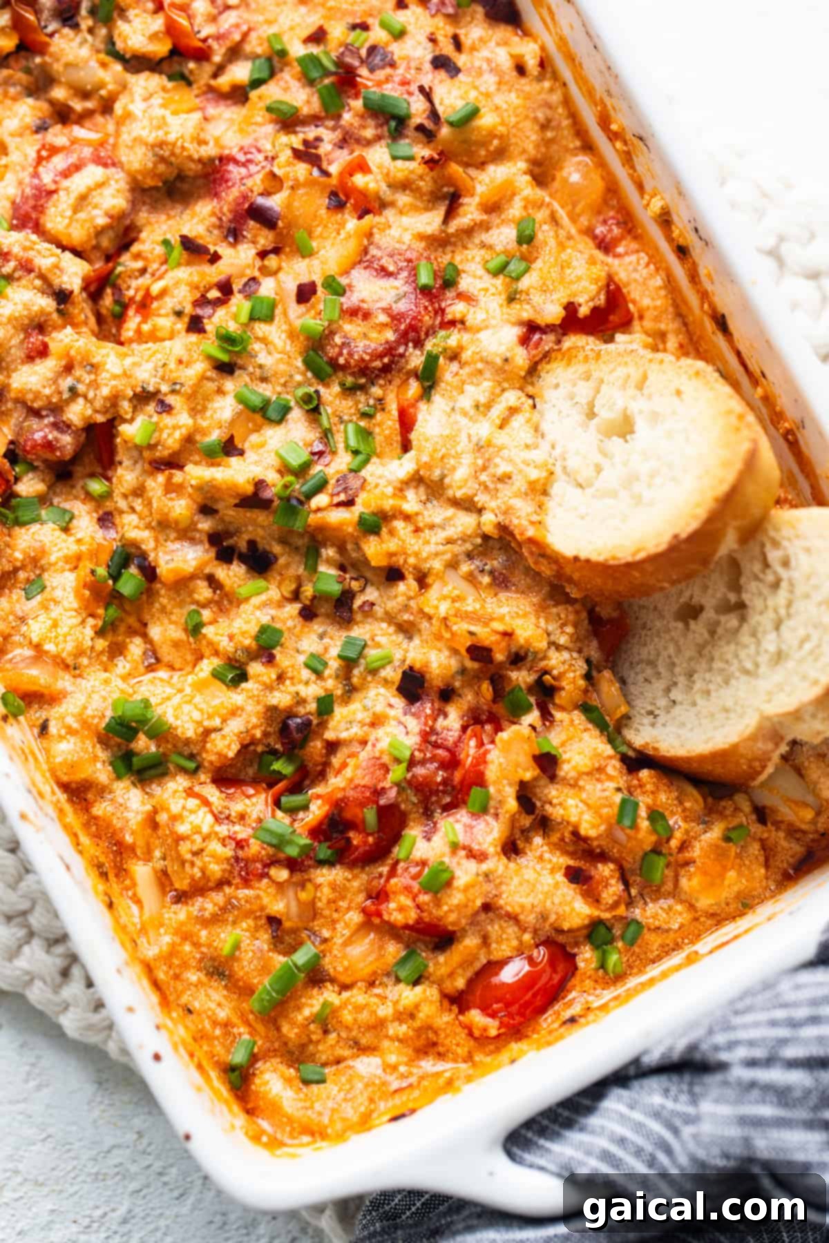 Irresistible Roasted Garlic Boursin Melt 2 A beautiful casserole dish filled with golden-brown baked Boursin dip, surrounded by glistening roasted cherry tomatoes and slices of crusty bread, ready for serving.