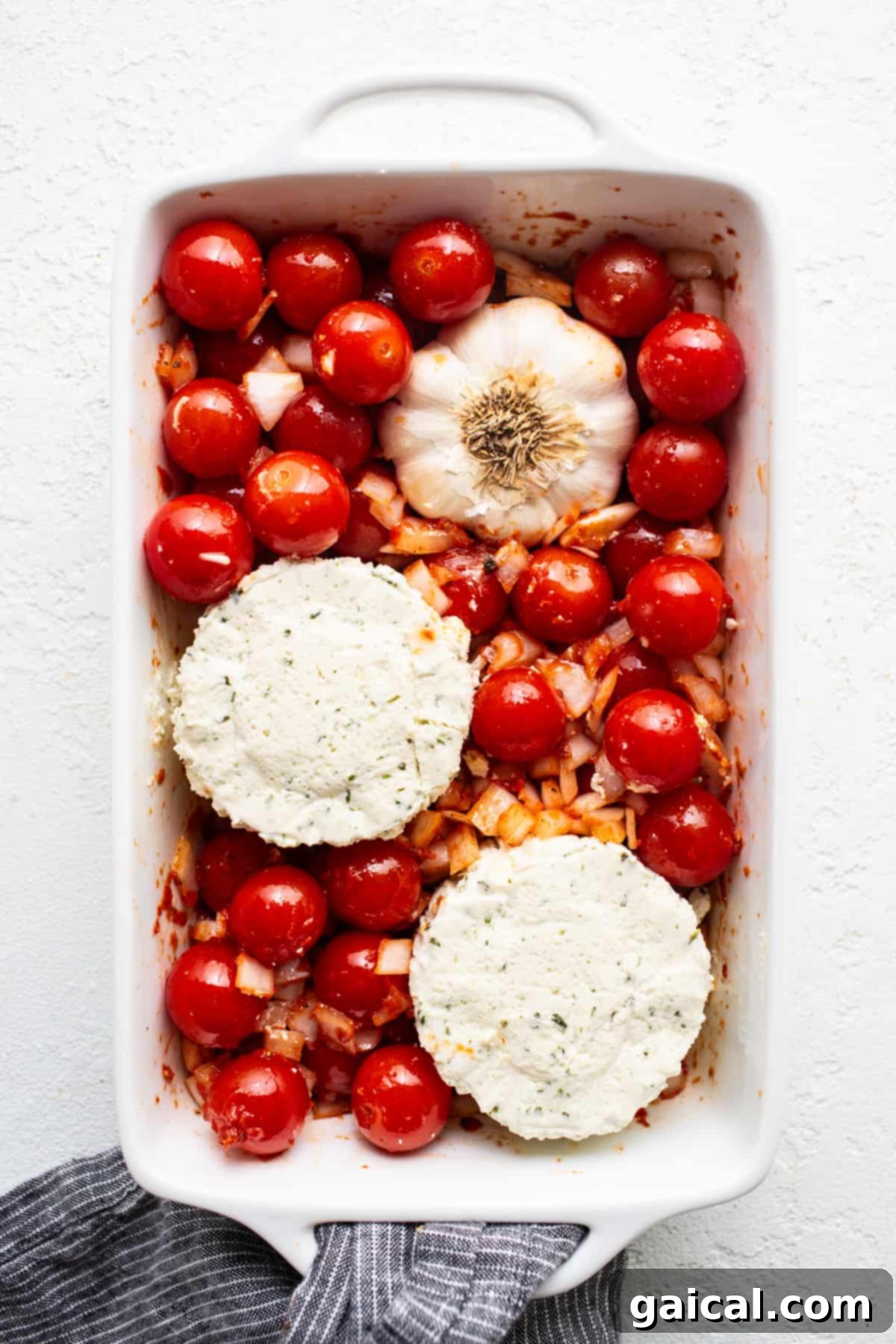 Irresistible Roasted Garlic Boursin Melt 4 A white baking dish filled with vibrant cherry tomatoes, golden garlic cloves, and creamy Boursin cheese before baking.