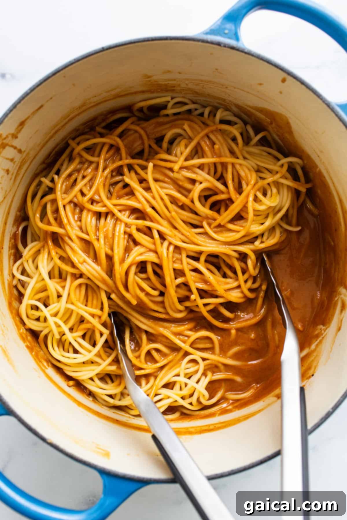 Freshly cooked spaghetti pasta being expertly lifted from a vibrant blue cooking pot with two forks, indicating it's perfectly al dente and ready to be sauced.