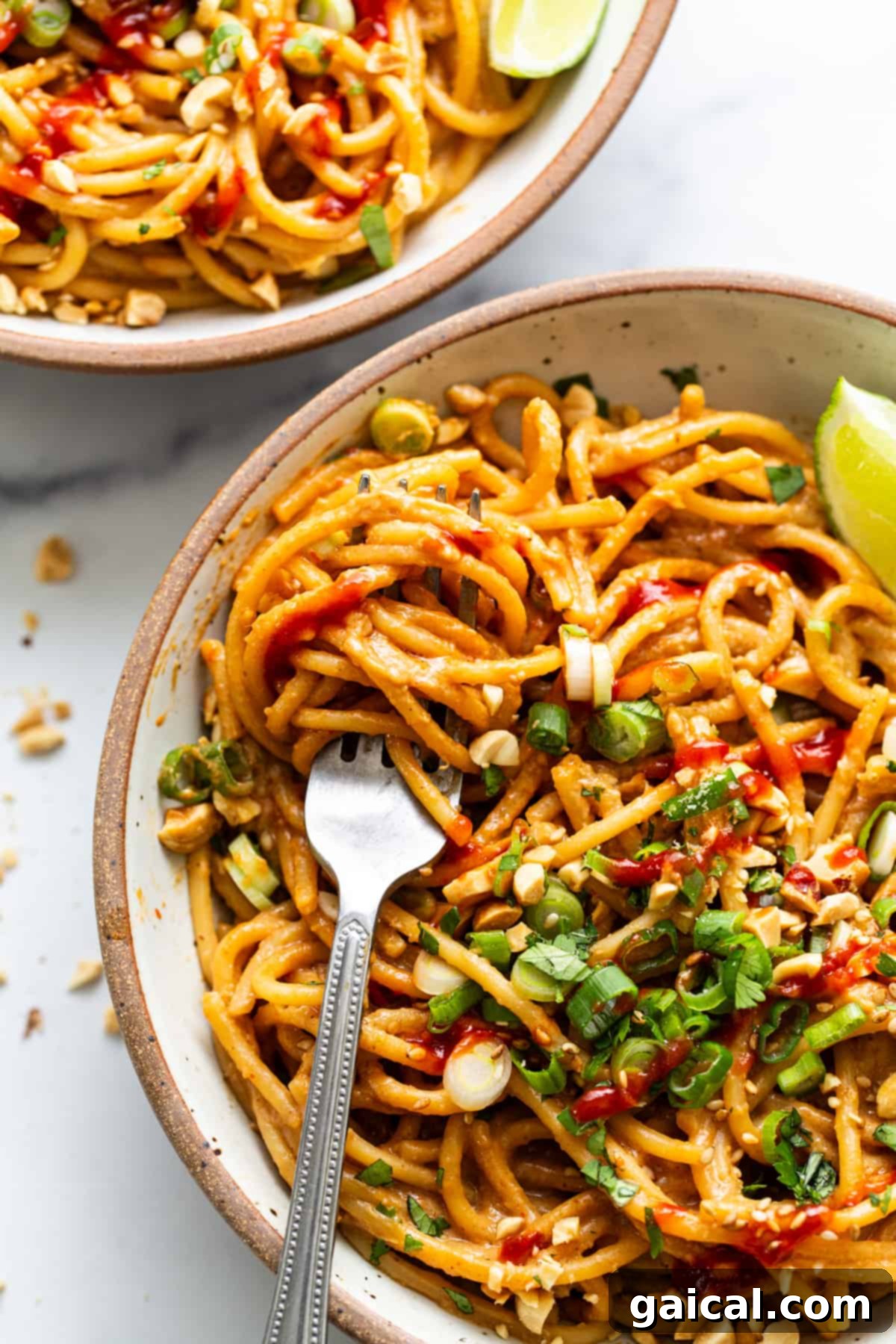 Two vibrant bowls of 20-Minute Thai Peanut Noodles, each beautifully garnished with fresh lime wedges, a sprinkle of chopped peanuts, and cilantro, artfully arranged on a light-colored surface.