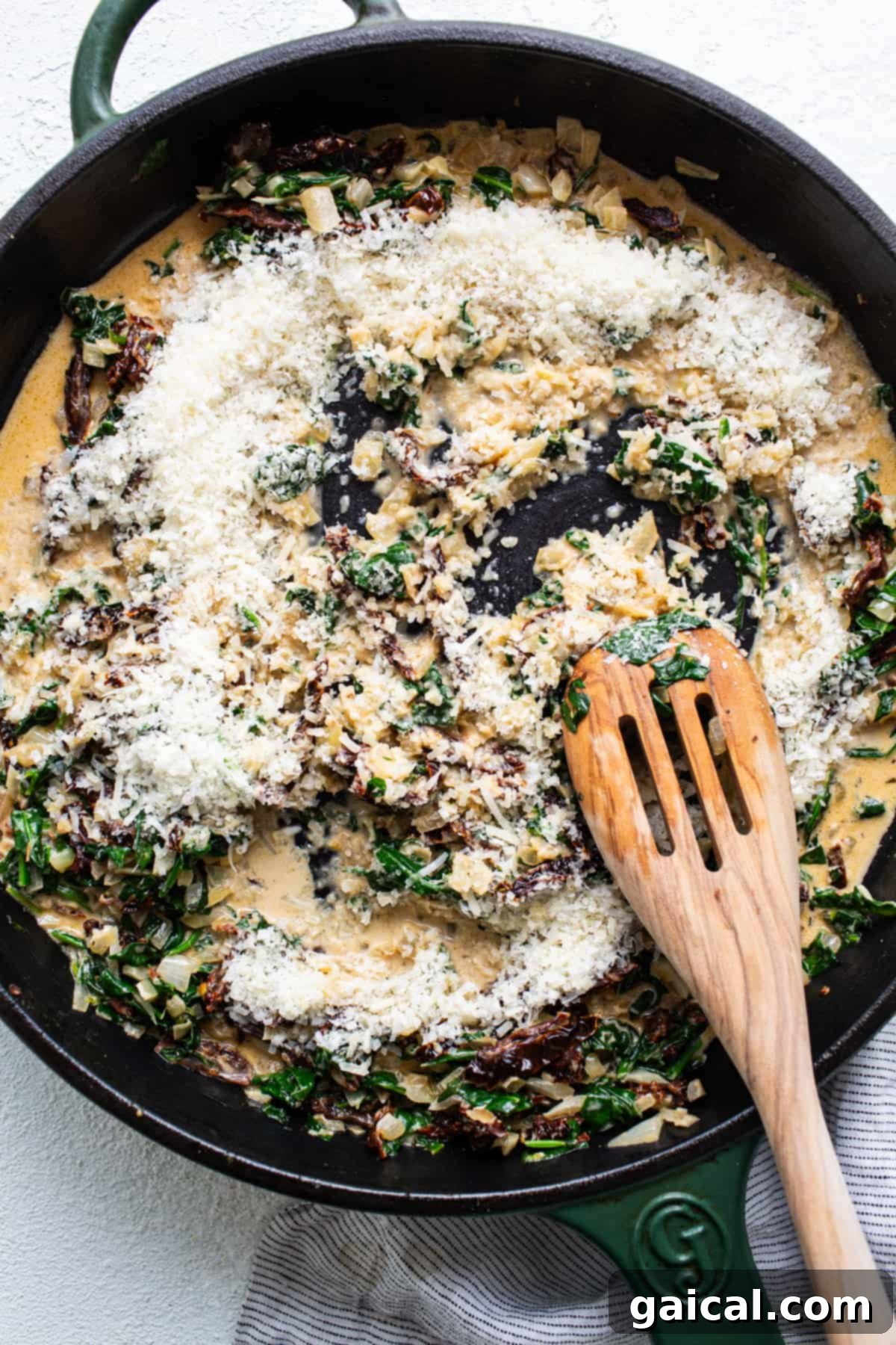 Creamy Tuscan Shrimp Linguini 12 A skillet filled with spinach and cheese with a wooden spoon.