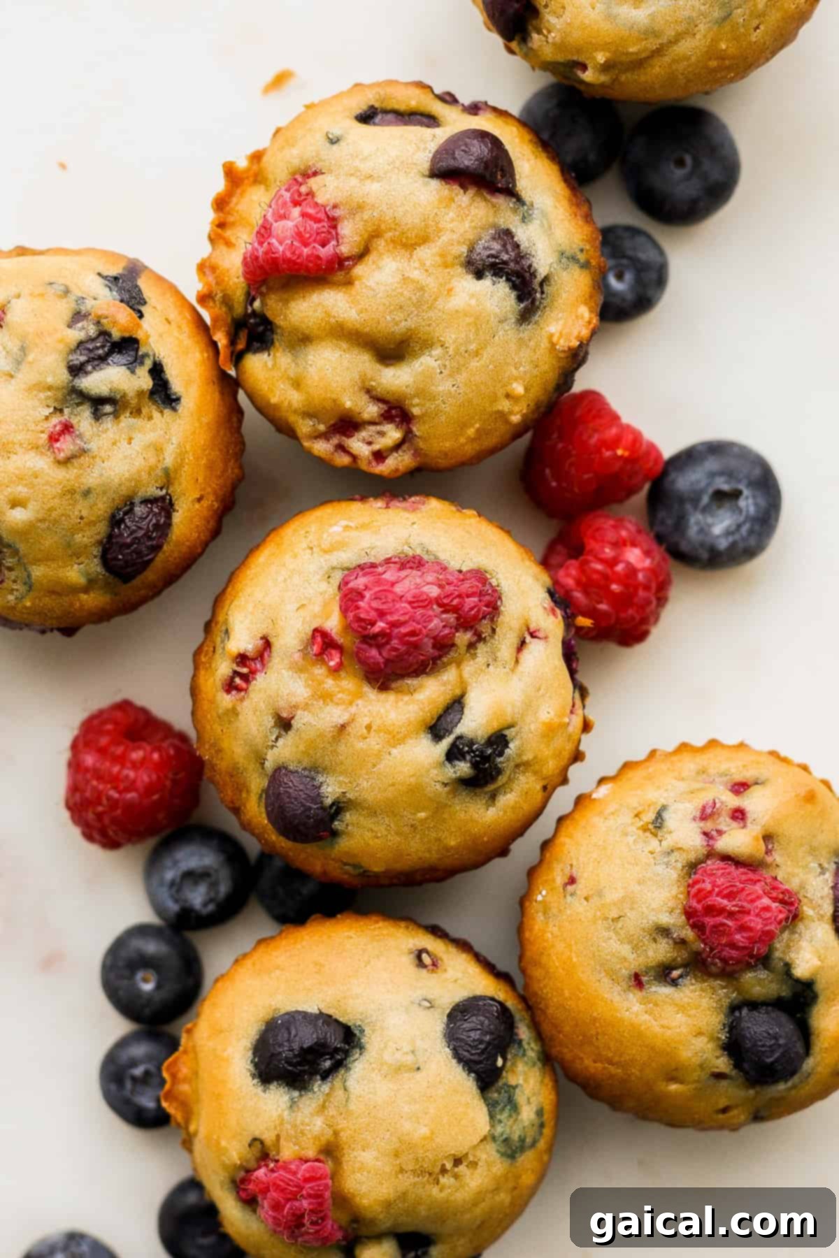 A vibrant cluster of fluffy Greek yogurt berry muffins, generously topped with fresh raspberries and blueberries, showcasing their golden-brown tops and moist texture.