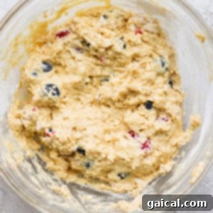 A close-up shot of muffin batter in a bowl, featuring visible blueberries and a thick, lumpy texture, indicating it's perfectly mixed.