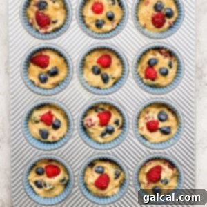 A muffin tin filled with freshly baked muffins, some topped with blueberries and raspberries, still hot from the oven.
