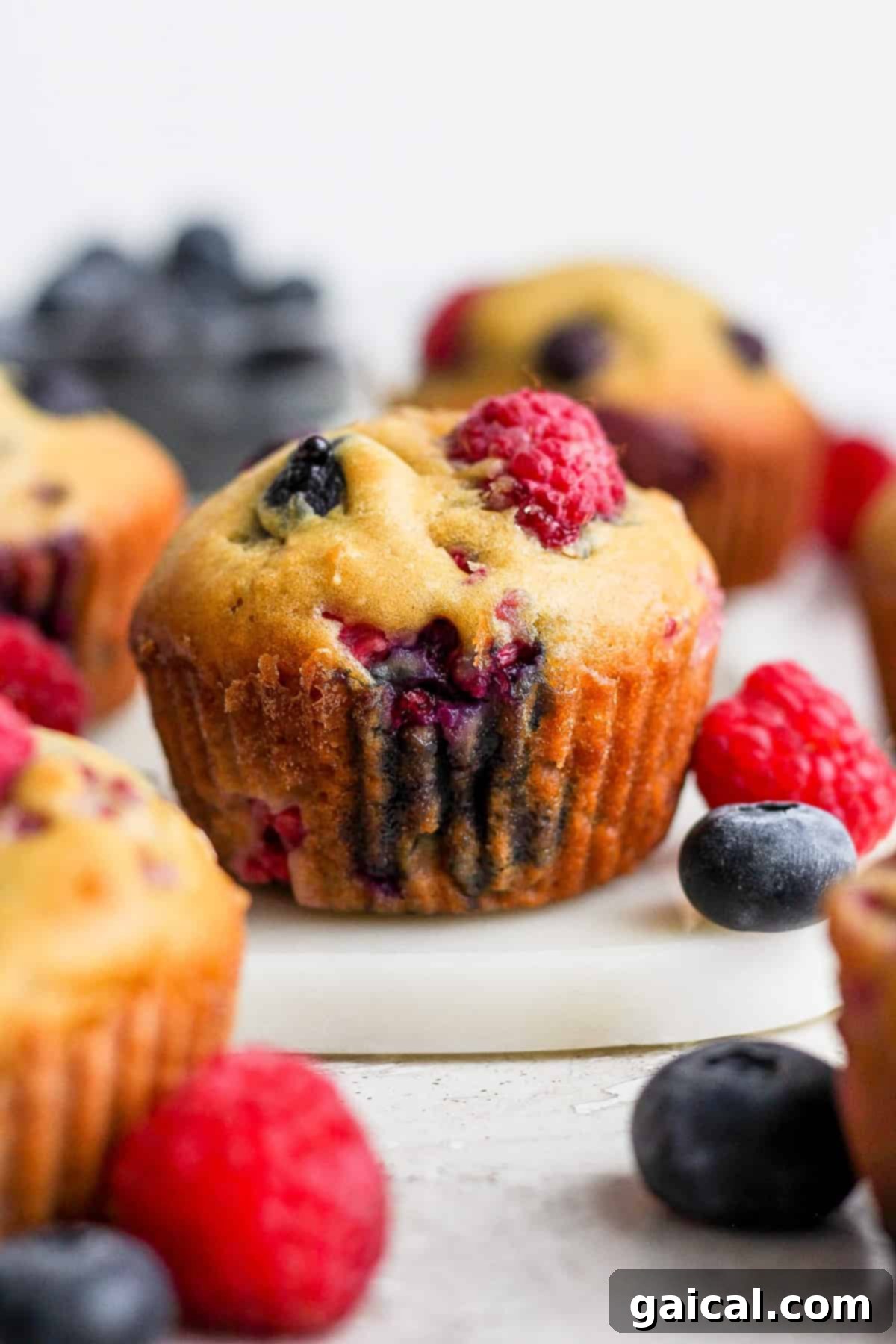 Delicious Greek yogurt berry muffins arranged on a rustic wooden cutting board, garnished with fresh blueberries and raspberries.