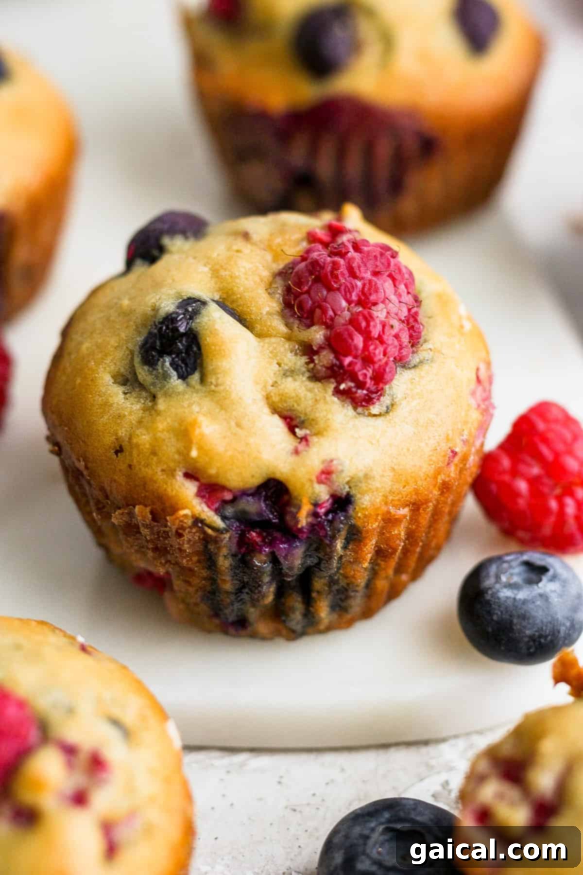 A perfectly baked Greek yogurt berry muffin, topped with vibrant blueberries and raspberries, resting on a clean white plate.