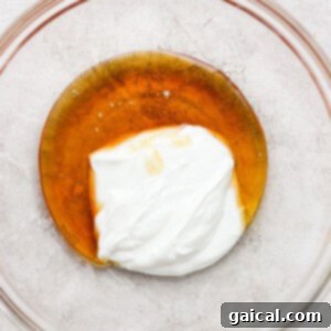 A glass bowl holds a creamy, pale mixture being whisked, showcasing the smooth blend of wet ingredients for the muffins.