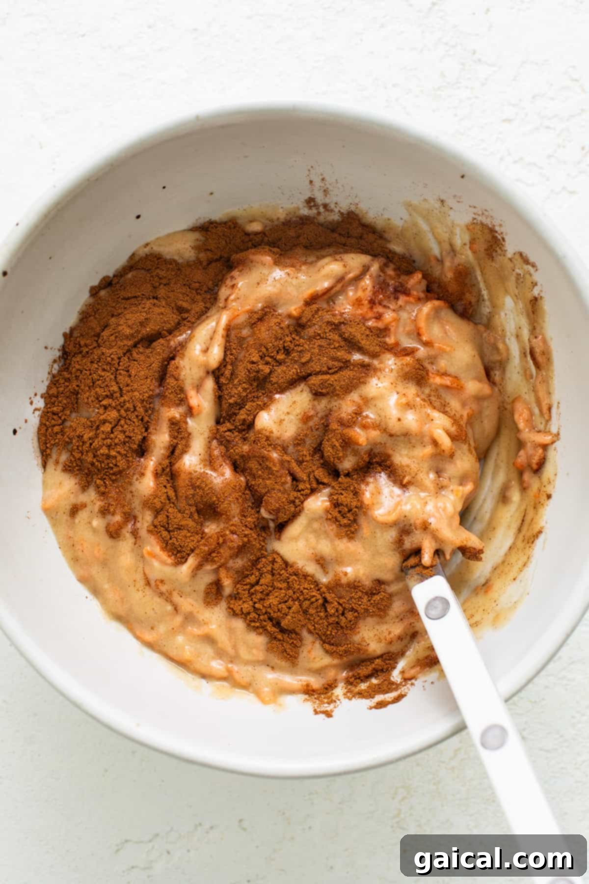 Spiced Carrot Coffee Cake 3 A white bowl with a spoon in it, showcasing a finely shredded carrot mixture, ready for baking.
