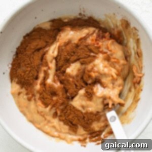 Spiced Carrot Coffee Cake 9 A white bowl with a spoon in it, showing the darker cinnamon batter.
