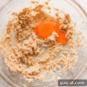 A glass bowl containing a mixture of flour and an egg, demonstrating the initial stages of combining cookie ingredients.