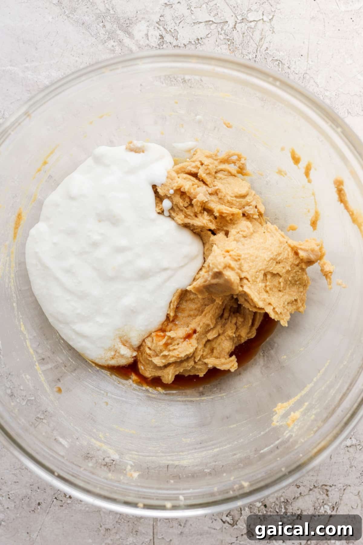 A clear glass bowl showcasing the carefully combined wet ingredients for cookie dough, including softened butter, rich brown sugar, and a vibrant egg yolk, ready for the next step.