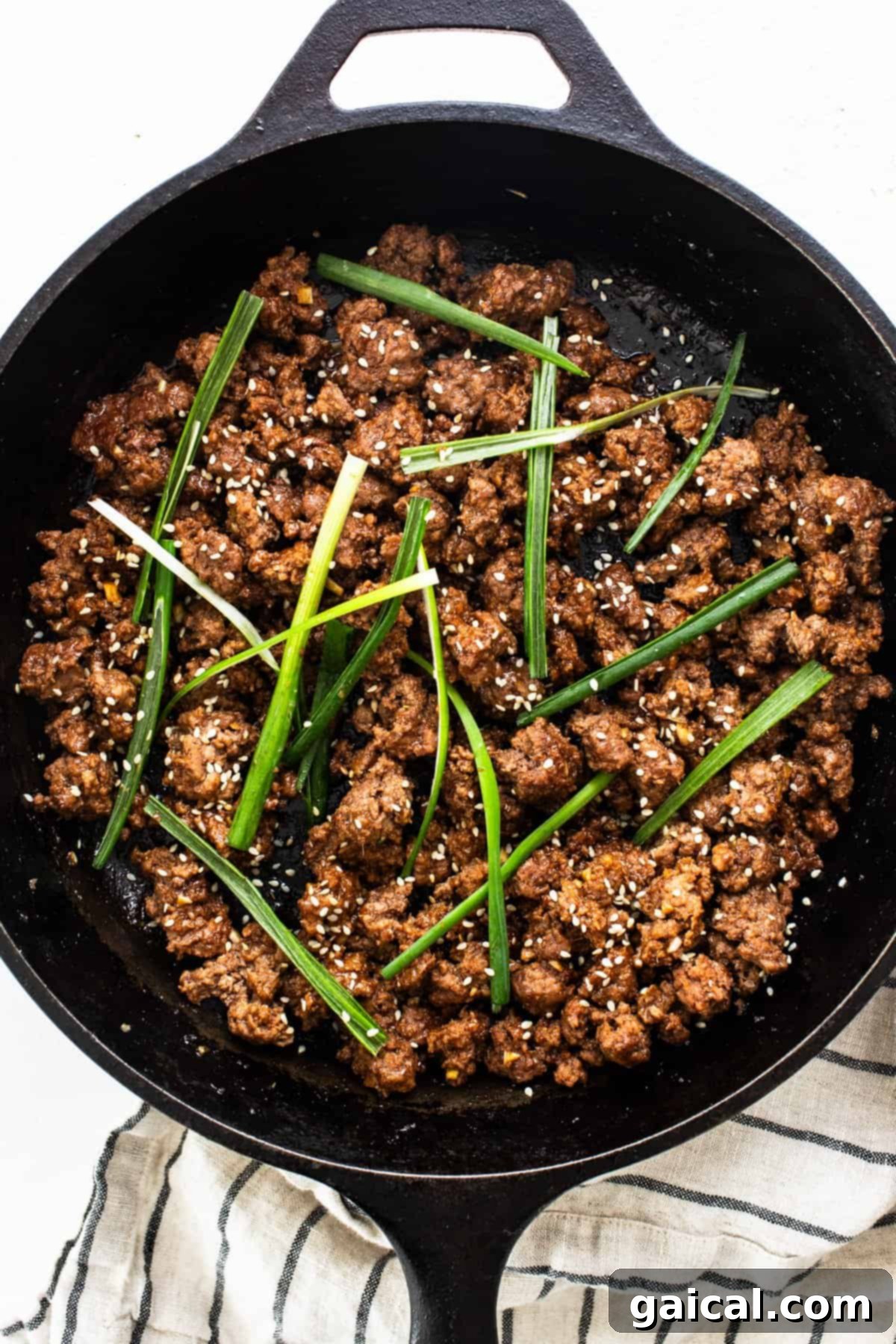 Sweet and Spicy Korean Ground Beef 3 Cooked Korean ground beef garnished with green onions and sesame seeds in a cast iron skillet.