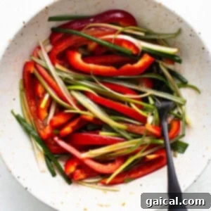 A bowl of sliced red bell peppers and green beans ready for cooking with Korean ground beef, accompanied by a spoon.
