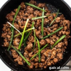 Cooked Korean ground beef garnished with green onions and sesame seeds in a cast iron skillet.