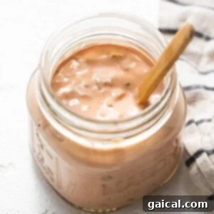 A jar of creamy homemade Thousand Island dressing with a wooden spoon.