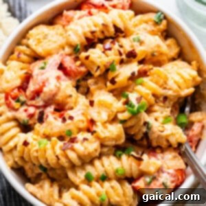 A bowl of creamy baked macaroni and cheese with sliced tomatoes and chopped green onions on top.