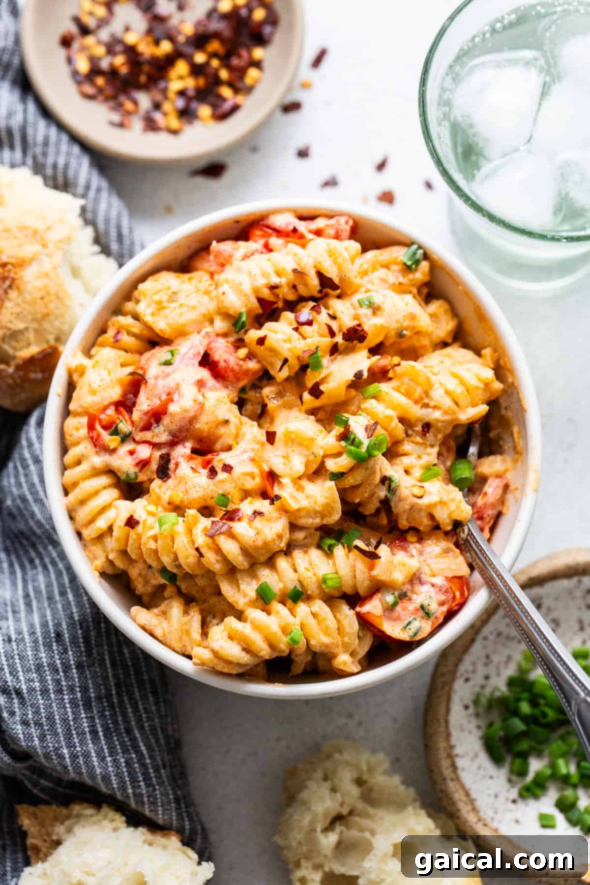 A bowl of creamy tomato pasta garnished with green onions, served with bread and a glass of water on the side.