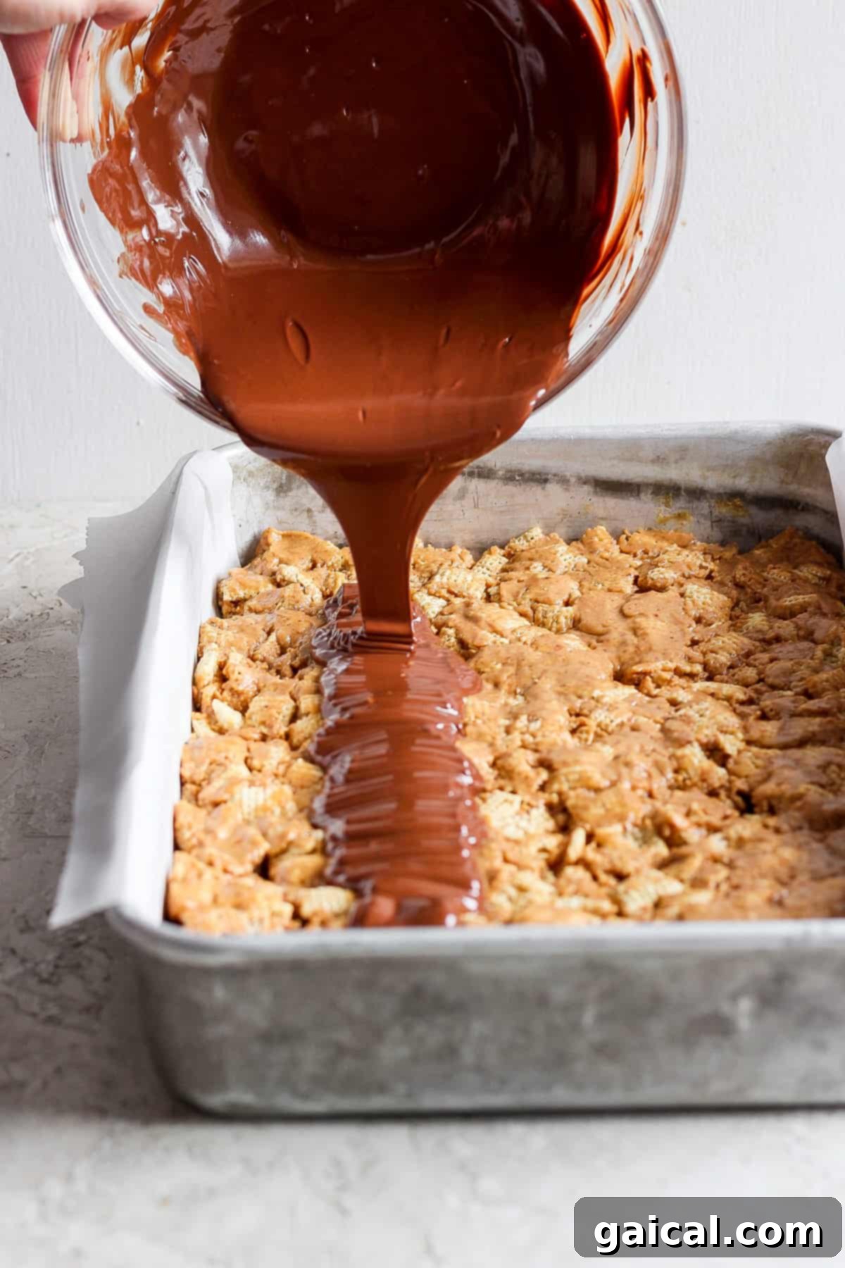 Chocolate sauce being poured onto a tray of baked dessert bars.