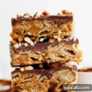 Stack of three peanut butter rice krispie treats topped with a layer of chocolate and sprinkled with chopped peanuts.