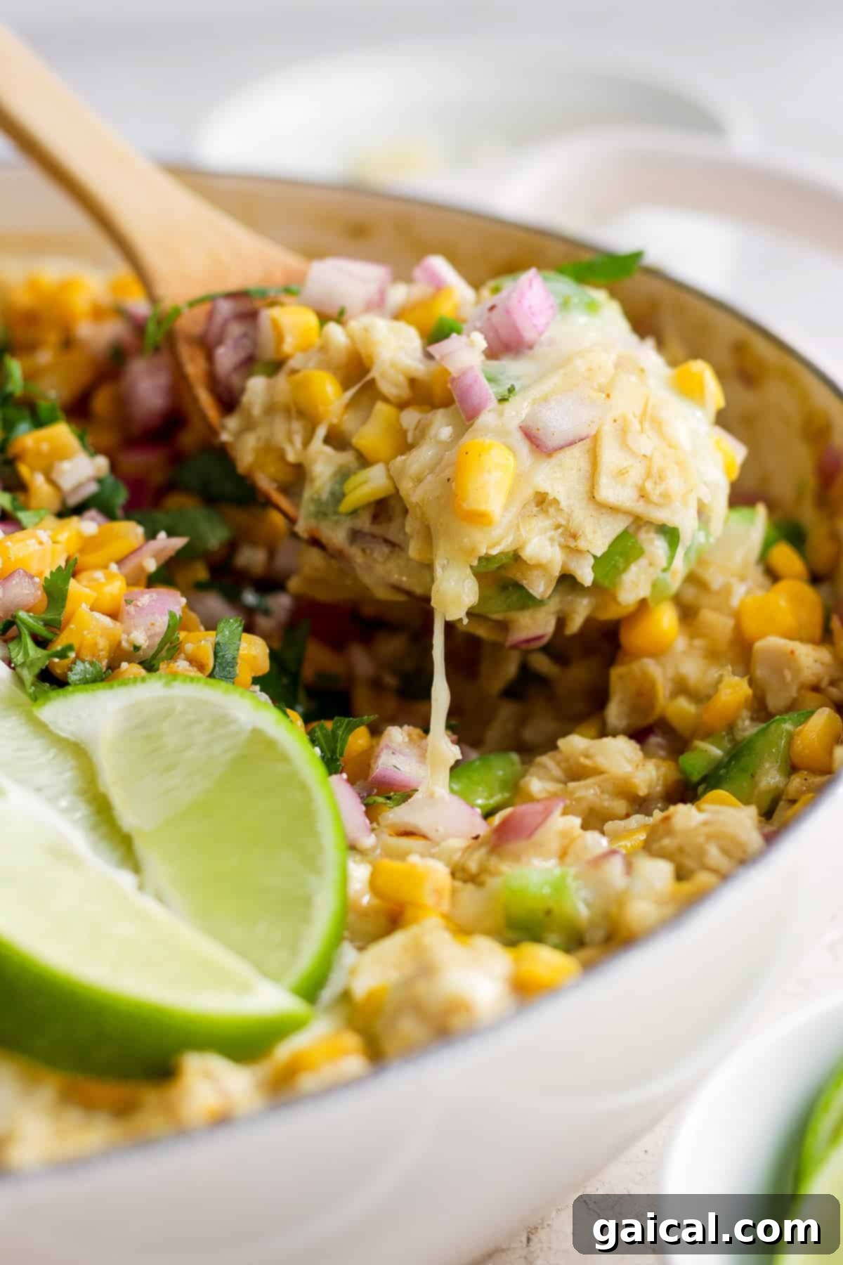 Mexican corn tortillas mixed with chicken and sauce in a pan with a wooden spoon.
