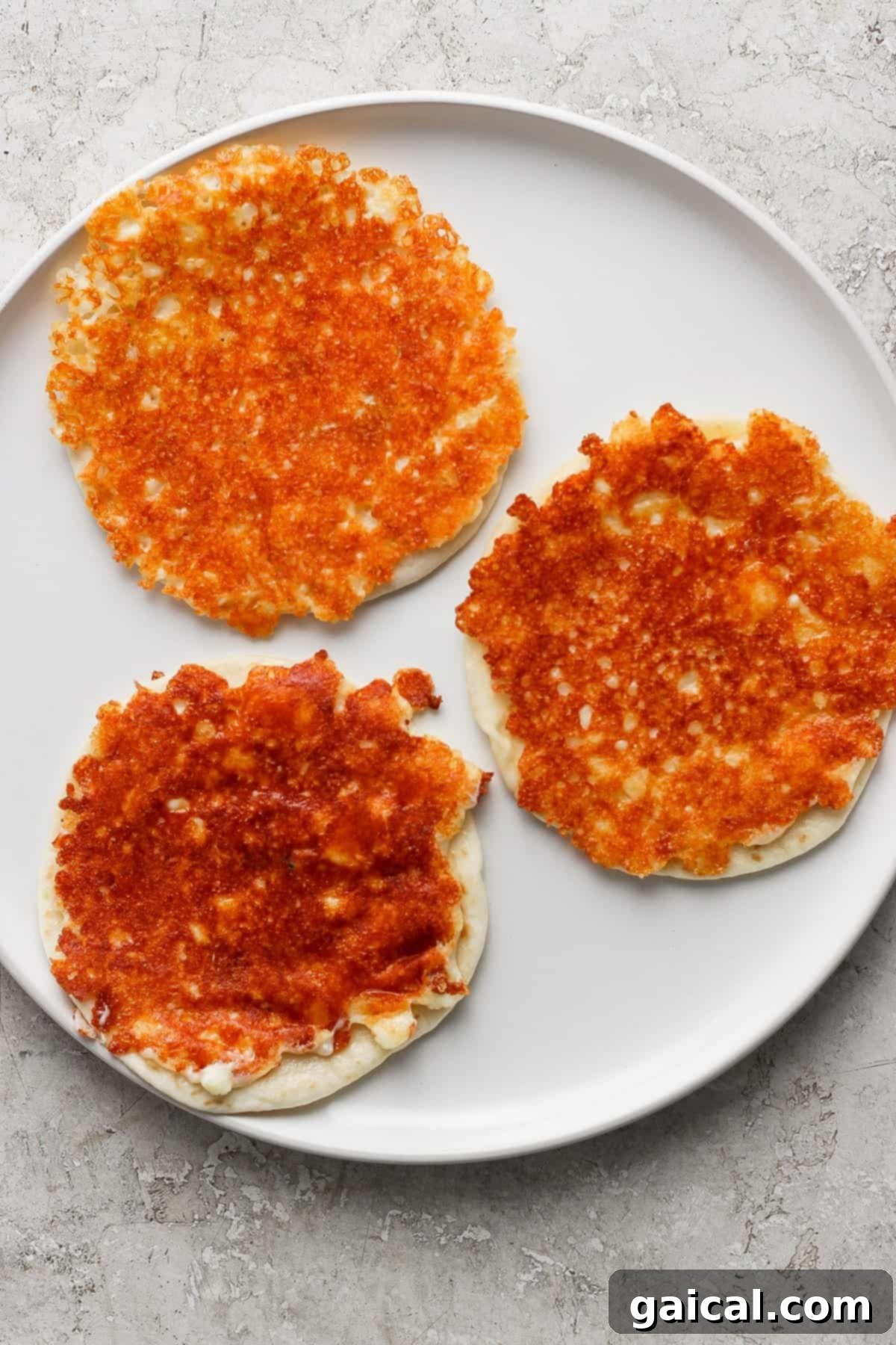 Zesty Cotija Chicken Tacos 3 Three golden-brown cheese pancakes on a white plate with a light textured background.