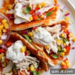 A plate of tacos with shredded chicken, corn, diced vegetables, and a dollop of sour cream served with a side of salsa.