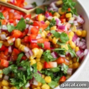 A vibrant bowl of corn salsa with diced red onions, chopped tomatoes, and fresh cilantro.