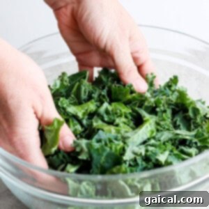 Vibrant Green Goddess Quinoa Bowl 11 A person is massaging kale in a glass bowl.