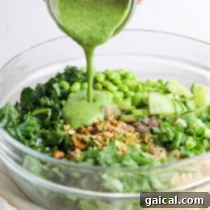 Vibrant Green Goddess Quinoa Bowl 12 Pouring a green dressing over a bowl of salad with kale, quinoa, cucumber, and green peas.