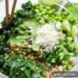 Vibrant Green Goddess Quinoa Bowl 13 A vibrant bowl of healthy greens consisting of avocado, edamame, kale, and chopped herbs with a quinoa base, topped with crumbled cheese and served with a green dressing, ready to be.