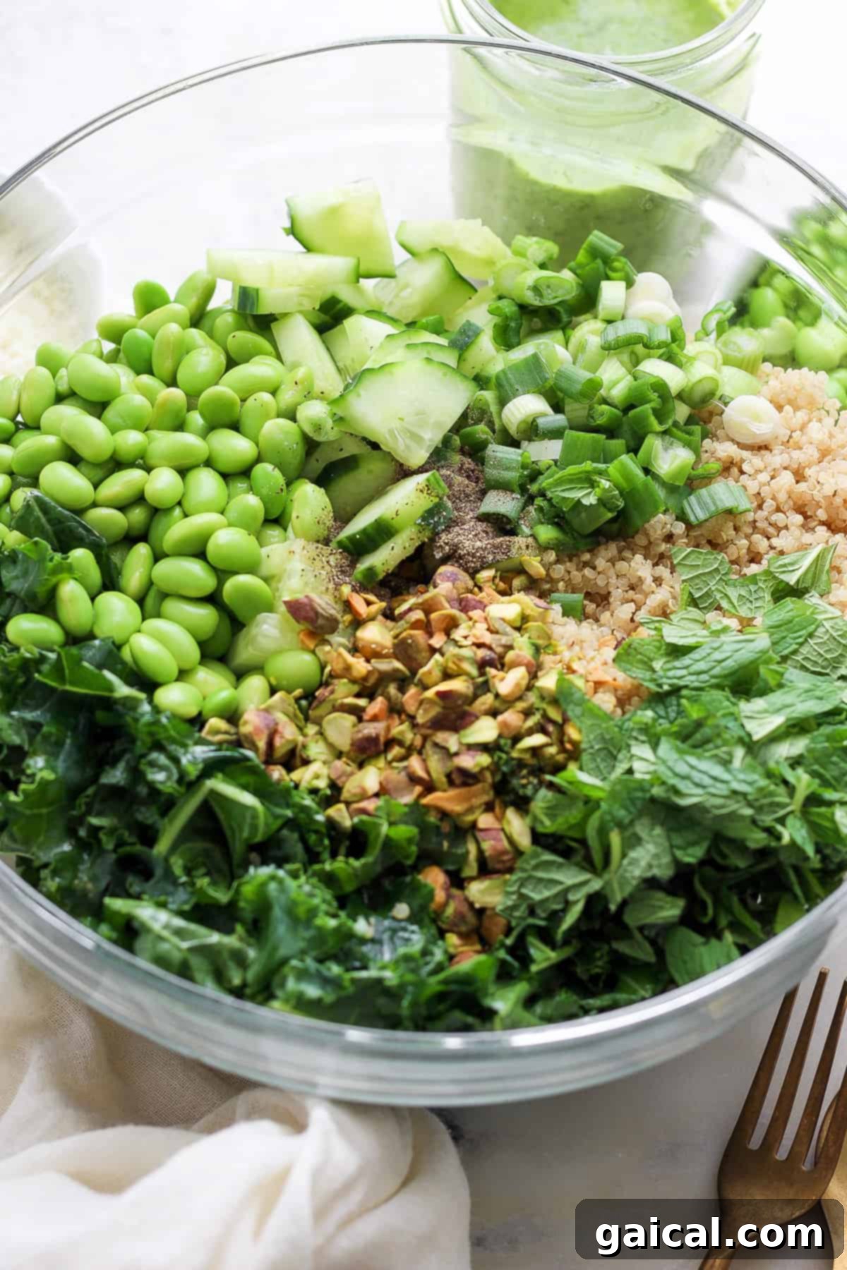 Vibrant Green Goddess Quinoa Bowl 5 A bowl containing a variety of fresh ingredients including greens, grains, cucumber, peas, chopped nuts, and herbs, likely prepared for a healthy salad.