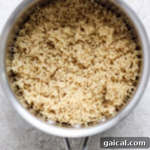 Vibrant Green Goddess Quinoa Bowl 8 A saucepan filled with cooked grains, possibly quinoa, on a textured surface.