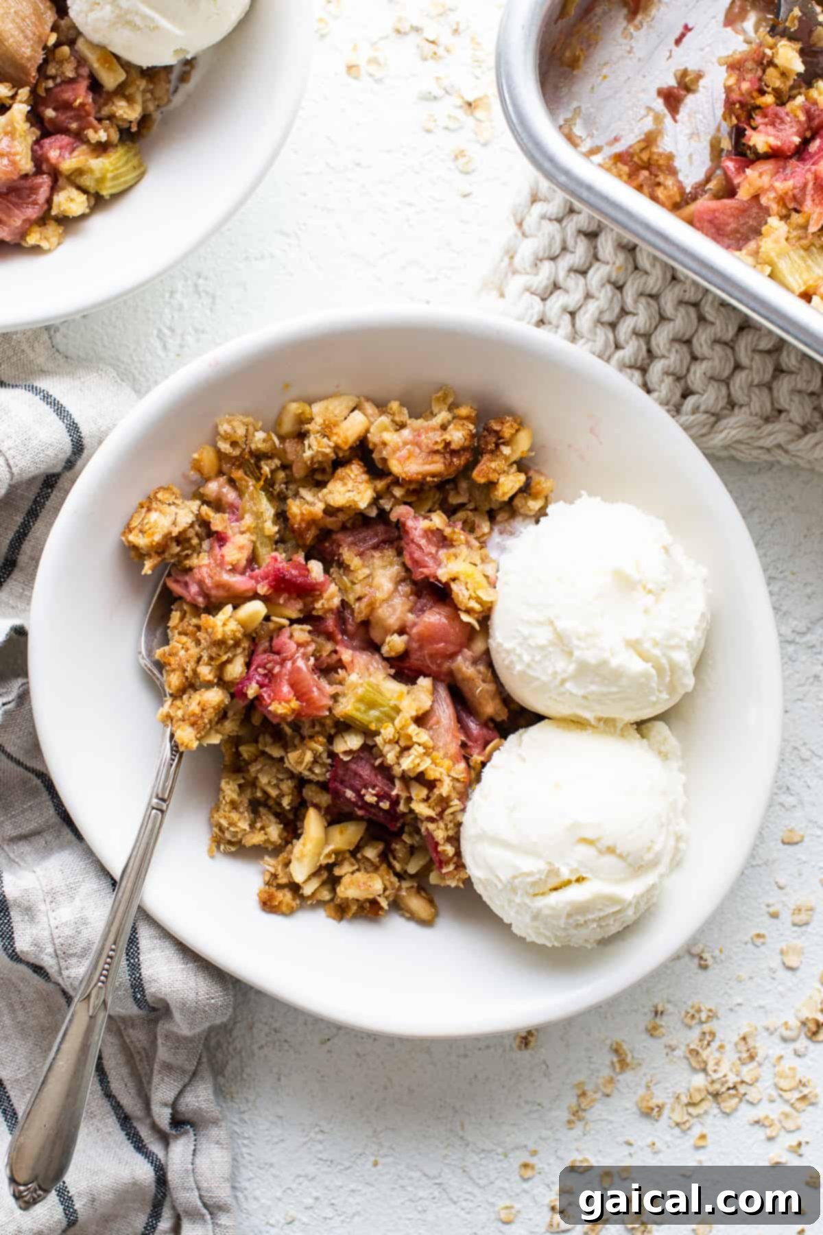 A bowl of vibrant rhubarb crisp, topped with a scoop of melting vanilla ice cream and fresh berries, ready to be enjoyed.