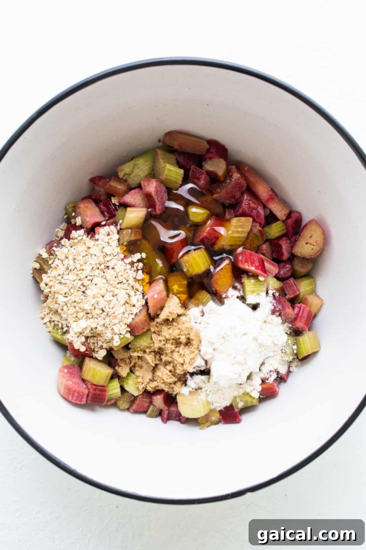 Freshly chopped rhubarb and quick-cooking oats in a mixing bowl on a white surface, ready for the crisp filling.