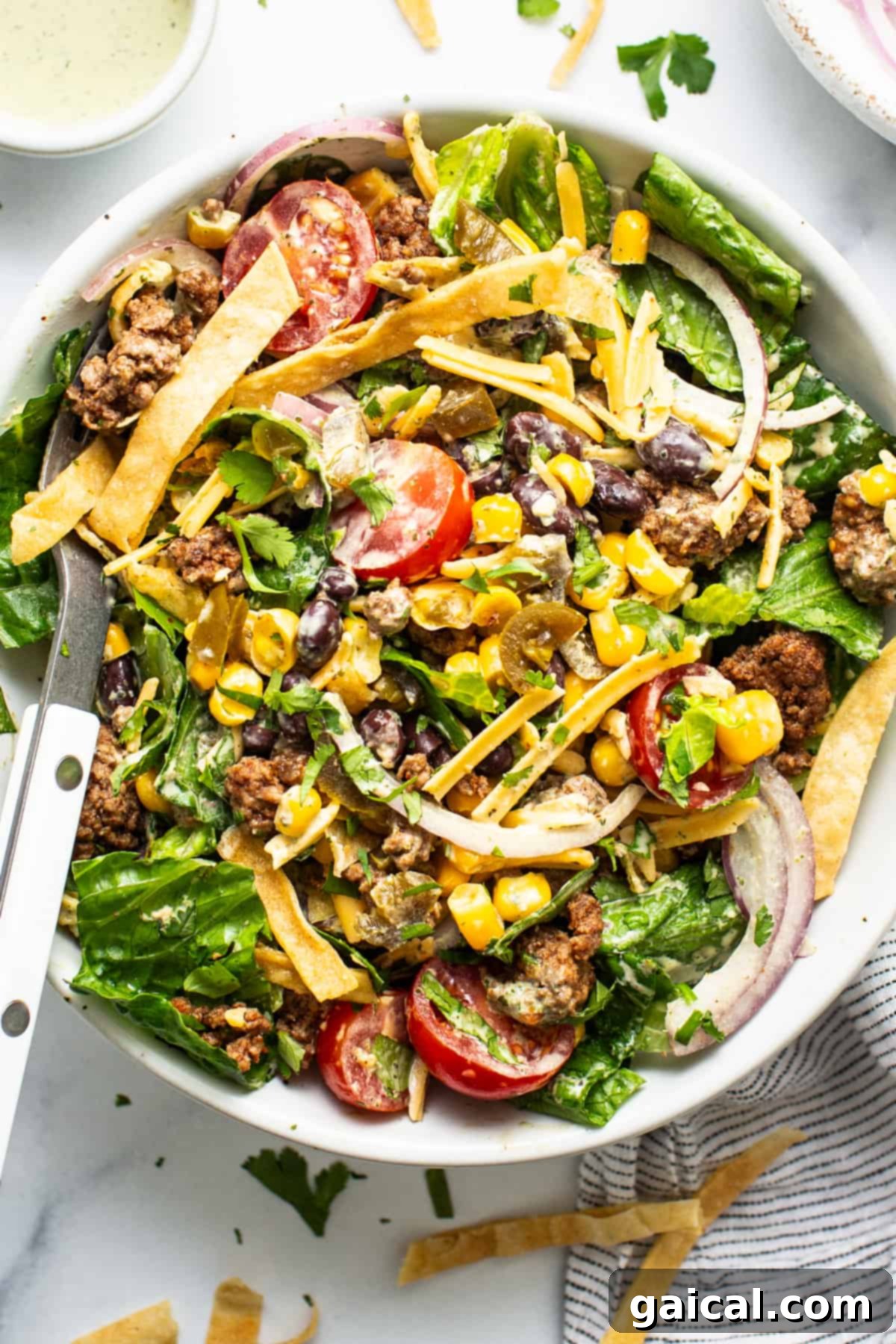 Meal Prep Taco Salad 2 A vibrant taco salad with ground meat, mixed greens, tomatoes, cheese, corn, black beans, and crispy tortilla strips, served with a creamy dressing on the side.
