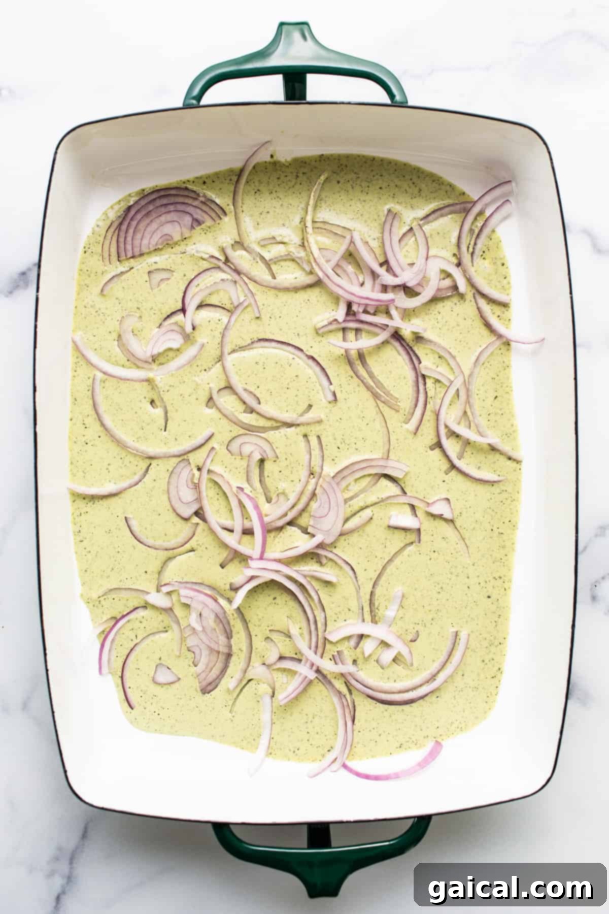 Meal Prep Taco Salad 3 A ceramic dish containing a creamy mixture topped with thinly sliced red onions.