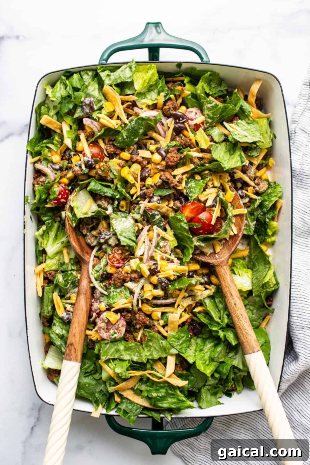 Meal Prep Taco Salad 6 A colorful mixed salad with various greens, nuts, cheese, and tomatoes served in a large green dish with wooden serving utensils.