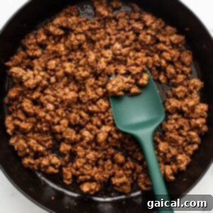 Cooked ground meat in a black cast iron skillet with a green spatula.