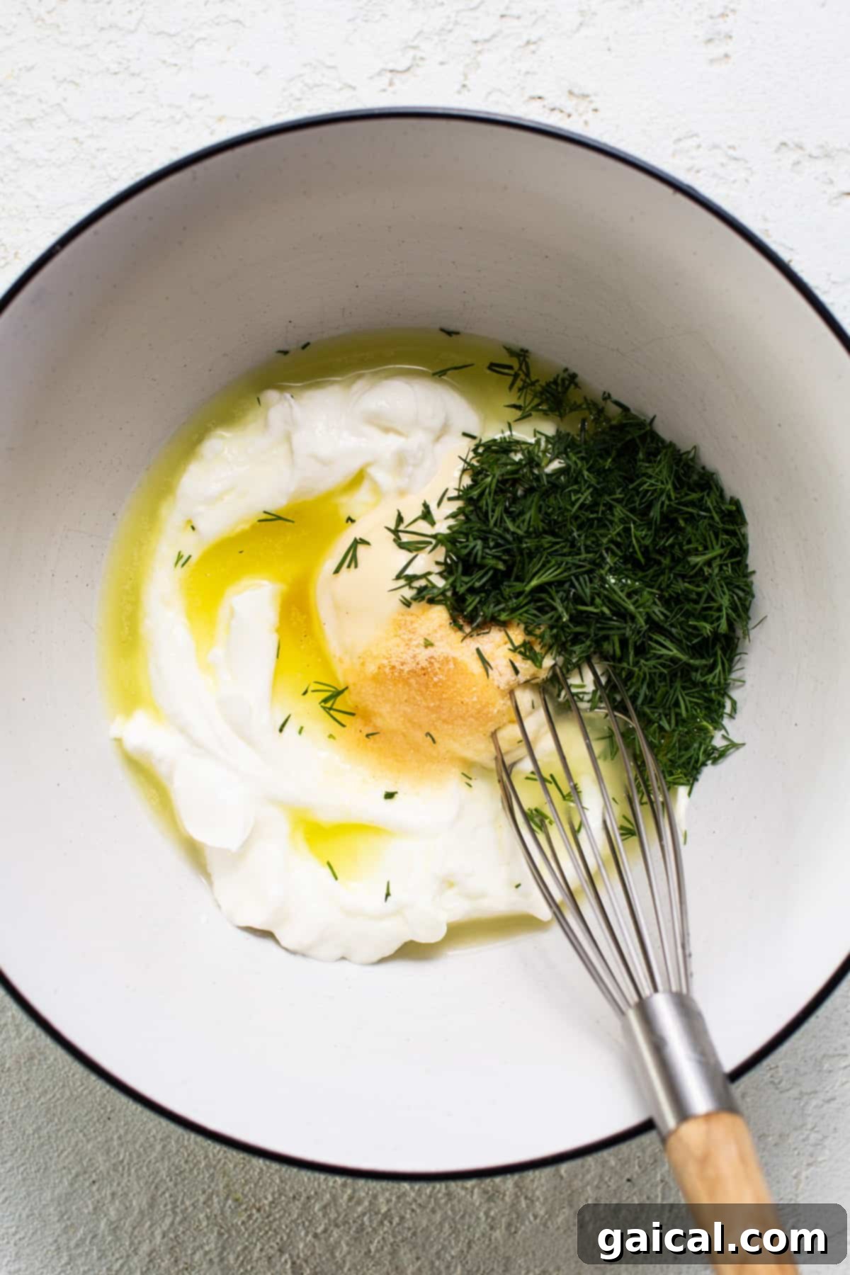 The perfectly prepared creamy sauce for the dill pickle chicken salad, expertly whisked in a transparent glass bowl, showcasing its smooth texture and vibrant flecks of fresh dill, poised and ready to be combined with the main ingredients.