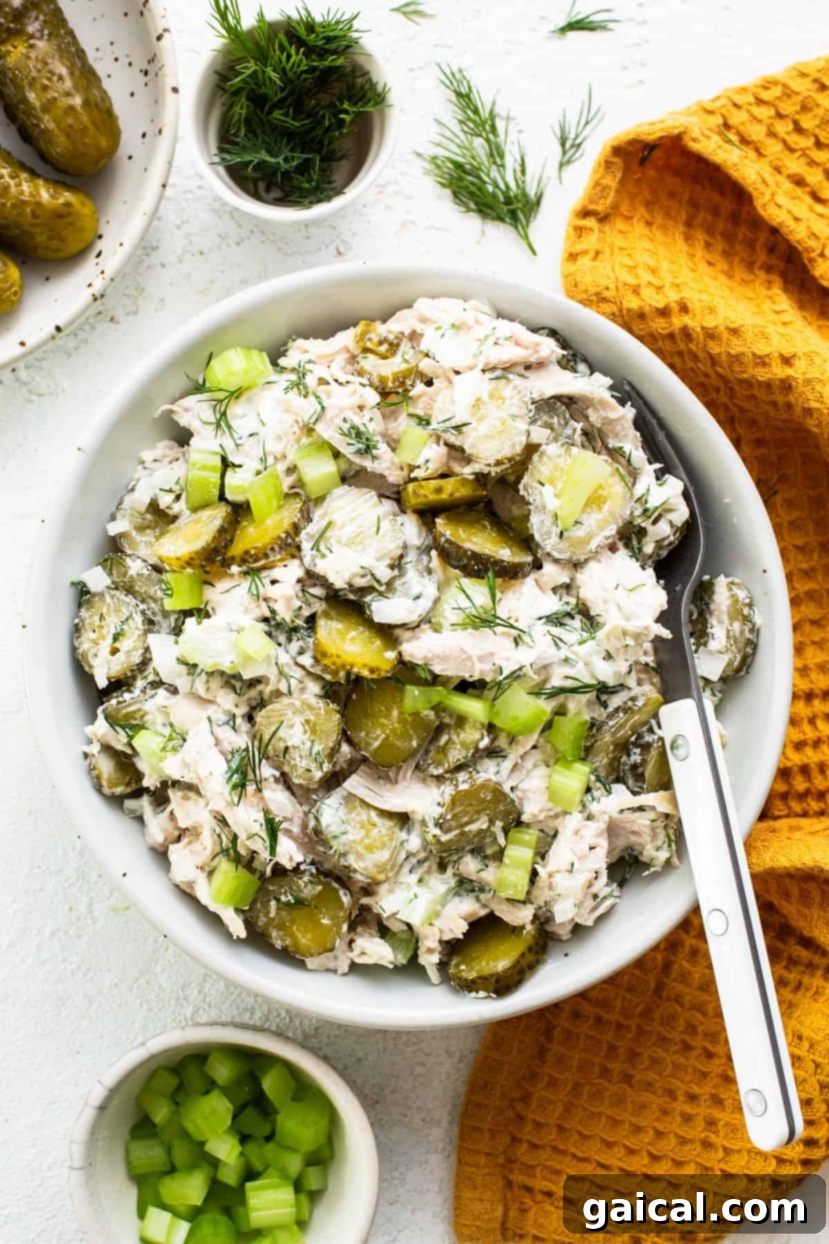 A mouth-watering close-up of dill pickle chicken salad generously spread on a piece of perfectly toasted artisan bread, elegantly garnished with fresh dill sprigs and surrounded by whole pickles and finely chopped celery, showcasing its irresistible texture, vibrant green accents, and appealing creaminess, ideal for a satisfying and healthy meal.