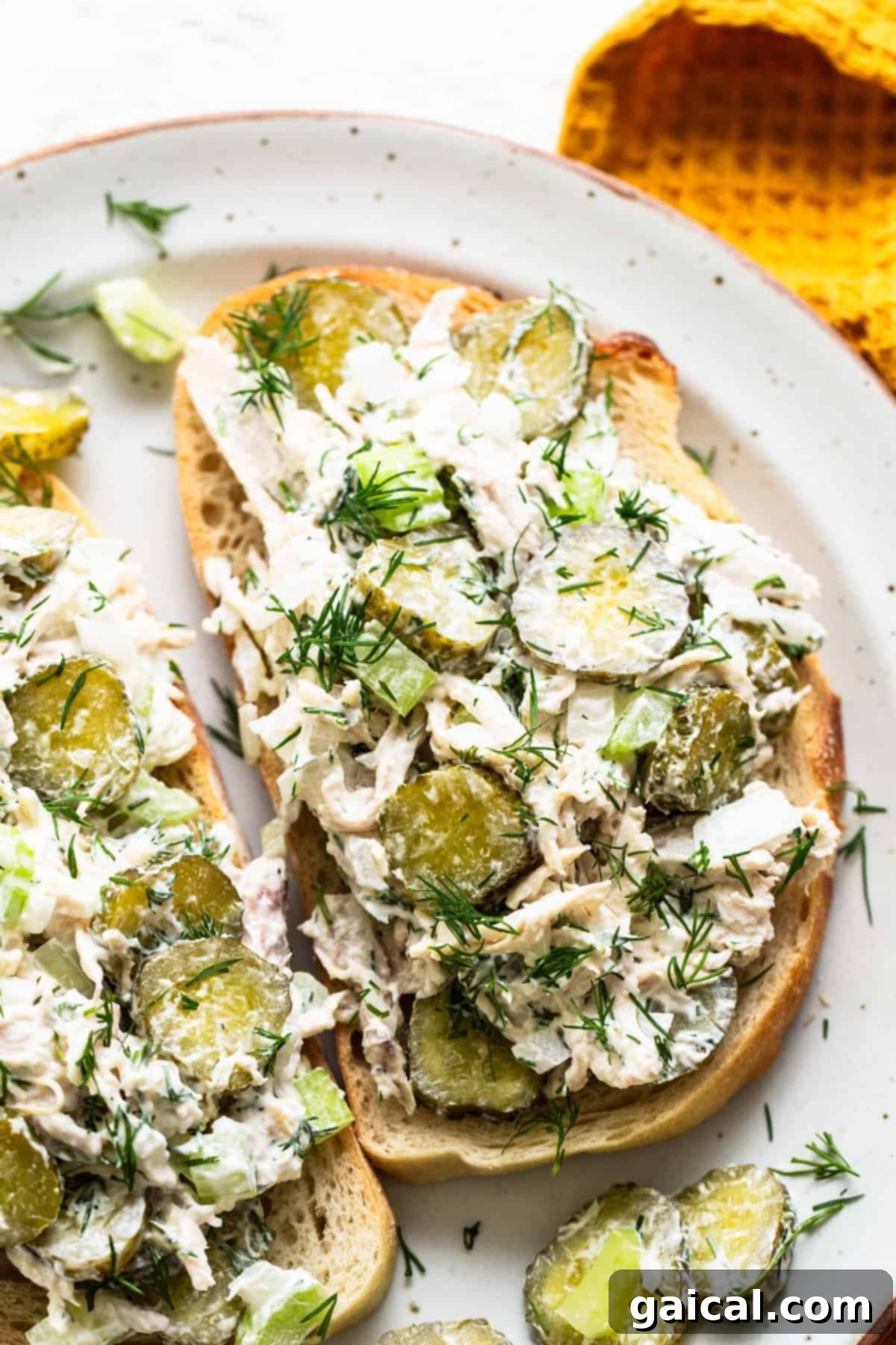A mouth-watering image of creamy dill pickle chicken salad generously spread on a piece of perfectly toasted artisan bread, exquisitely garnished with fresh dill sprigs and surrounded by whole pickles, highlighting the inviting texture, vibrant green accents, and overall appeal, making it an ideal choice for a satisfying and healthy meal.
