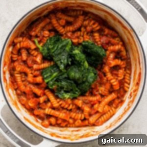 One-Pot Wonder Vodka Pasta 10 Pasta in tomato sauce with spinach mixed in, cooking in a white pot, reaching al dente perfection.