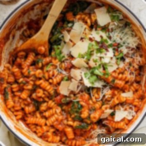 One-Pot Wonder Vodka Pasta 11 A pot of tomato-based pasta, mixed with spinach and garnished with a generous amount of grated cheese and fresh herbs, ready to be served.