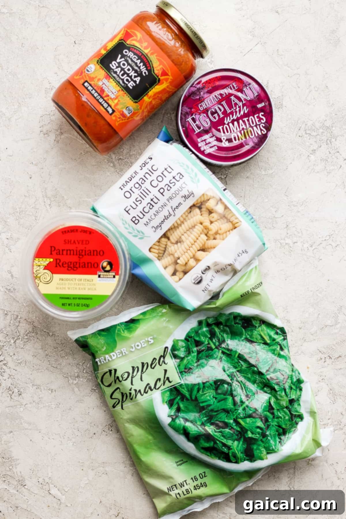 One-Pot Wonder Vodka Pasta 3 An array of fresh and packaged ingredients from Trader Joe's, including rich tomato sauce, diced tomatoes, gnocchi, shaved Parmesan cheese, and frozen chopped spinach, neatly arranged for cooking.